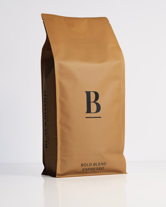 Roasted coffee beans. Blackboard Coffee Roasters, Blackboard Bold Espresso Blend. Image shows a matte sand coloured 1kg bag against a white background. The bag features the Blackboard logo centred in the middle of the bag and the blend name centred at the bottom. The Roast Collective.