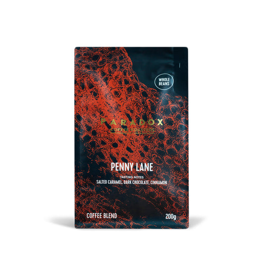 Roasted coffee beans from The Roast Collective. Paradox Coffee Roasters, Penny Lane Blend. Image shows a 200g bag of the coffee against a white background. The bag is two-tone in colour, with navy blue and rust red arranged in a crocodile skin pattern. Paradox's logo is centred in the top half of the bag, with the blend name, tasting notes and weight underneath.