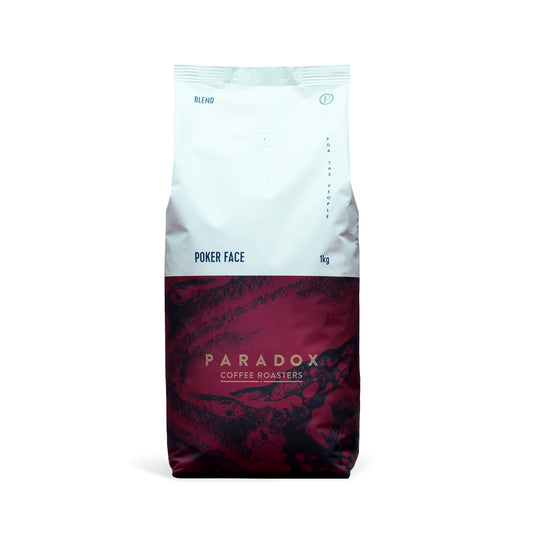 Roasted coffee beans from The Roast Collective. Paradox Coffee Roasters, Poker Face Blend. Image shows a tri-tone 1kg bag of the coffee against a white background. The top half of the bag is white, with a midnight blue and maroon pattern covering the bottom half of the bag. Paradox's logo is centred in the bottom half of the bag, with the lend name and weight at the bottom of the white section of the bag.