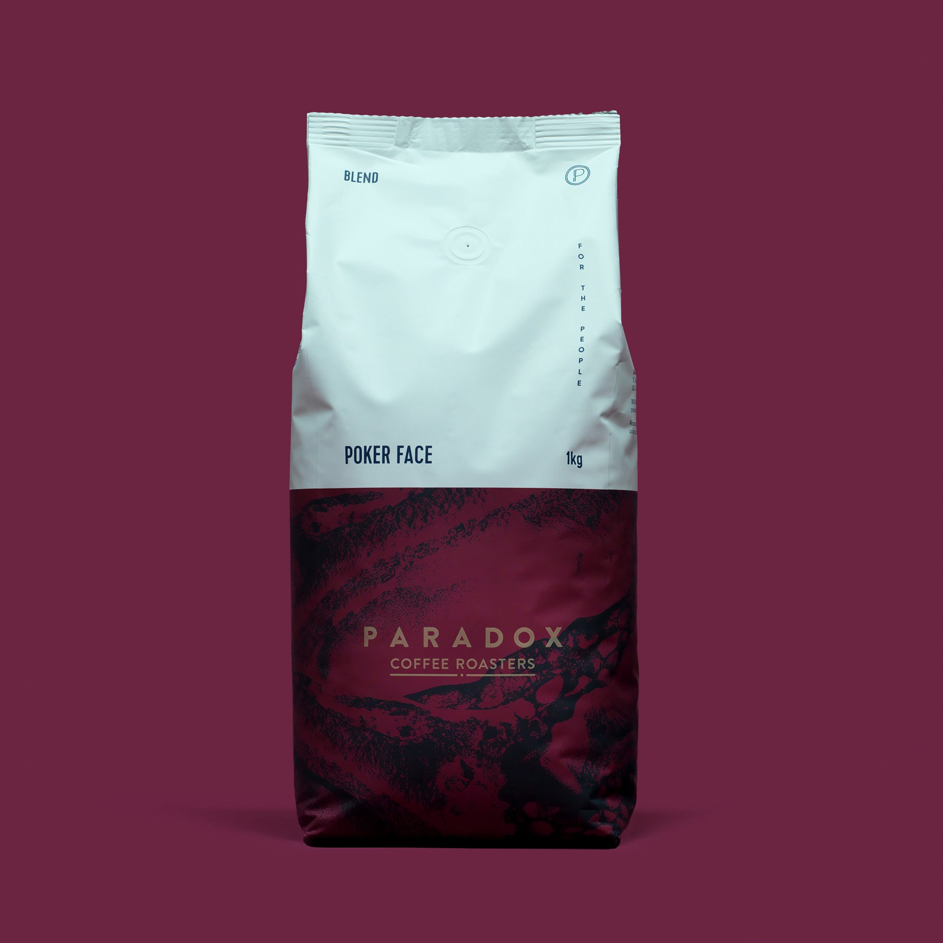 Roasted coffee beans from The Roast Collective. Paradox Coffee Roasters, Poker Face Blend. Image shows a tri-tone 1kg bag of the coffee against a maroon coloured background. The top half of the bag is white, with a midnight blue and maroon pattern covering the bottom half of the bag. Paradox's logo is centred in the bottom half of the bag, with the lend name and weight at the bottom of the white section of the bag.