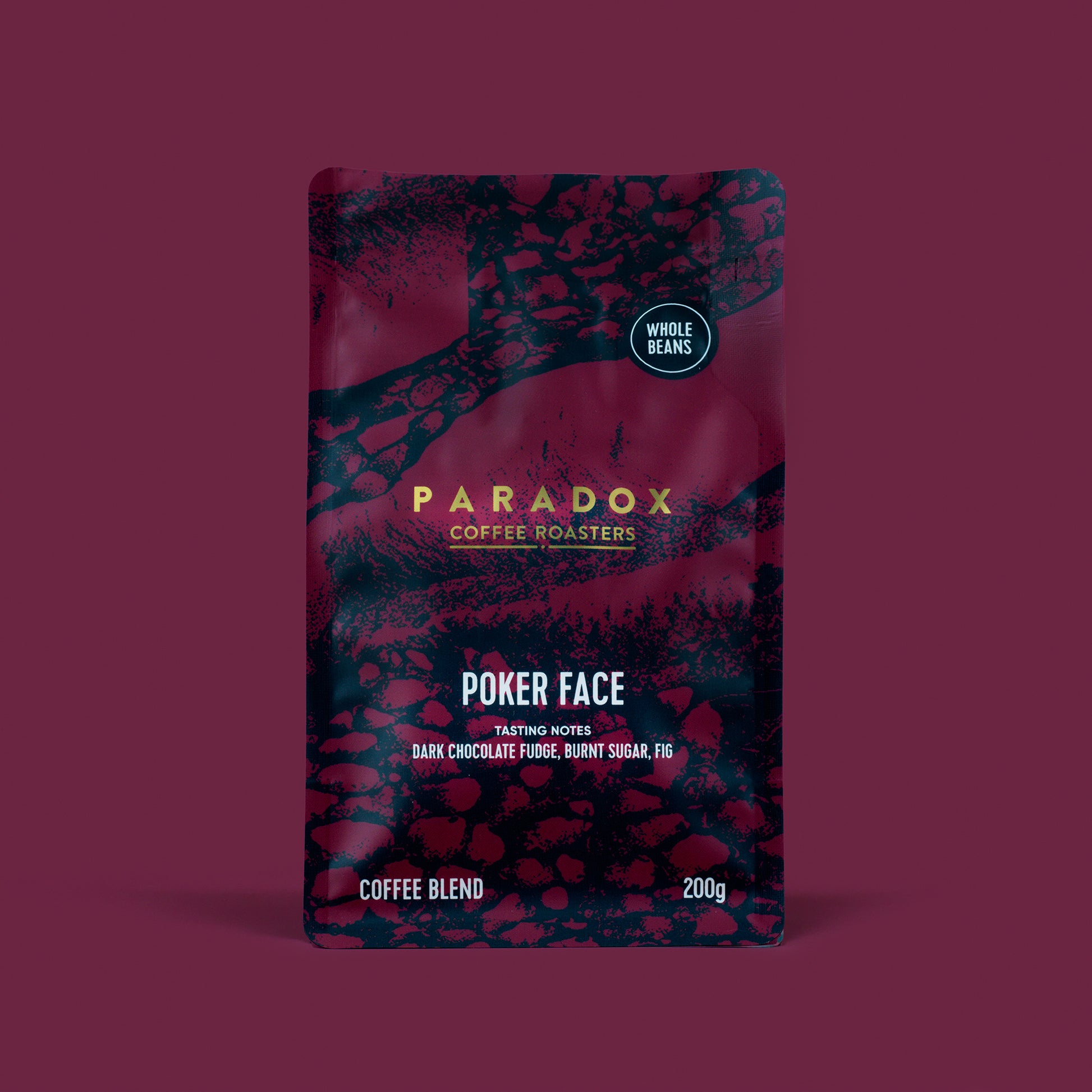 Roasted coffee beans from The Roast Collective. Paradox Coffee Roasters, Poker Face Blend. Image shows a 200g bag of the coffee against a maroon coloured background. The bag is two-tone in colour, with midnight blue and maroon arranged in a reptile skin pattern. Paradox's logo is centred in the top half of the bag, with the blend name, tasting notes and weight underneath.