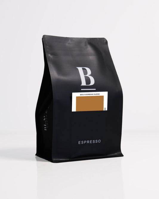 Roasted coffee beans. Blackboard Coffee Roasters, Blackboard Bold Espresso Blend. Image shows a black 250g bag against a white background. The bag features the Blackboard logo and a pouch on the front with a product information card poking out. The Roast Collective.