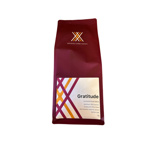 Roasted coffee beans. Extraction Coffee Roasters, Gratitude Blend. Image shows a 1kg bag of gratitude blend on a white background. The bag is maroon in colour. The Roast Collective