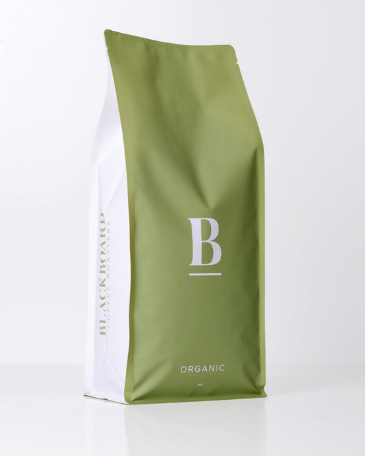 Roasted coffee beans. Blackboard Coffee Roasters, Blackboard Organic Espresso Blend. Image shows a green and white coloured 1kg bag against a white background. The bag features the Blackboard logo centred in the middle of the bag and the blend name centred at the bottom. The Roast Collective.