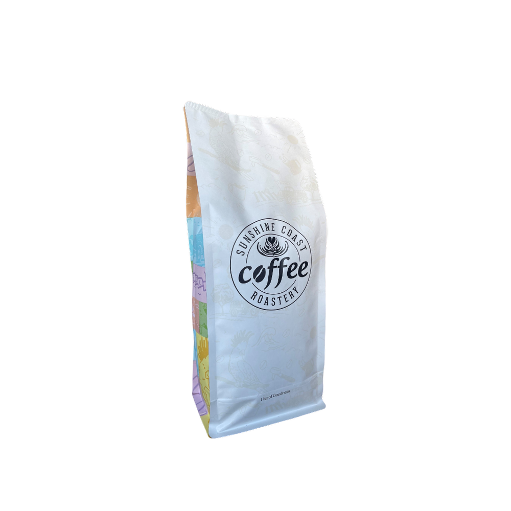 Roasted coffee beans from The Roast Collective. Sunshine Coast Coffee Roastery, Sunset Blend. Image shows a white 1kg bag of Sunset blend against a white background. The bag has the roaster's logo centred on the front of the bag with the brand's multicoloured theme on the sides of the bag. 