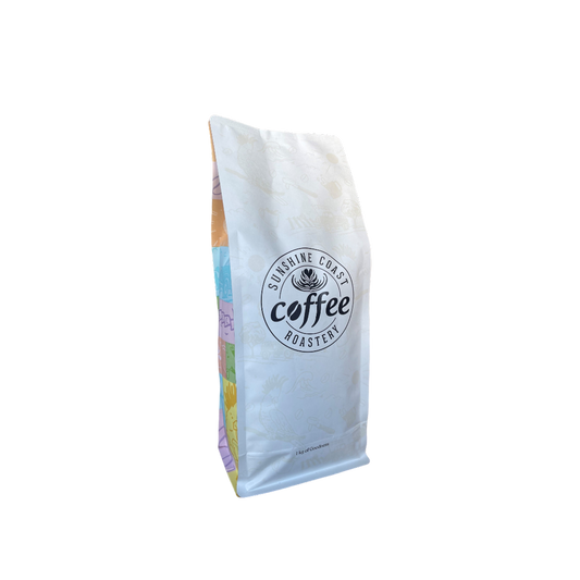 Roasted coffee beans from The Roast Collective. Sunshine Coast Coffee Roastery, Rumba Blend. Image shows a white 1kg bag of Rumba blend against a white background. The bag has the roaster's logo centred on the front of the bag with the brand's multicoloured theme on the sides of the bag. 
