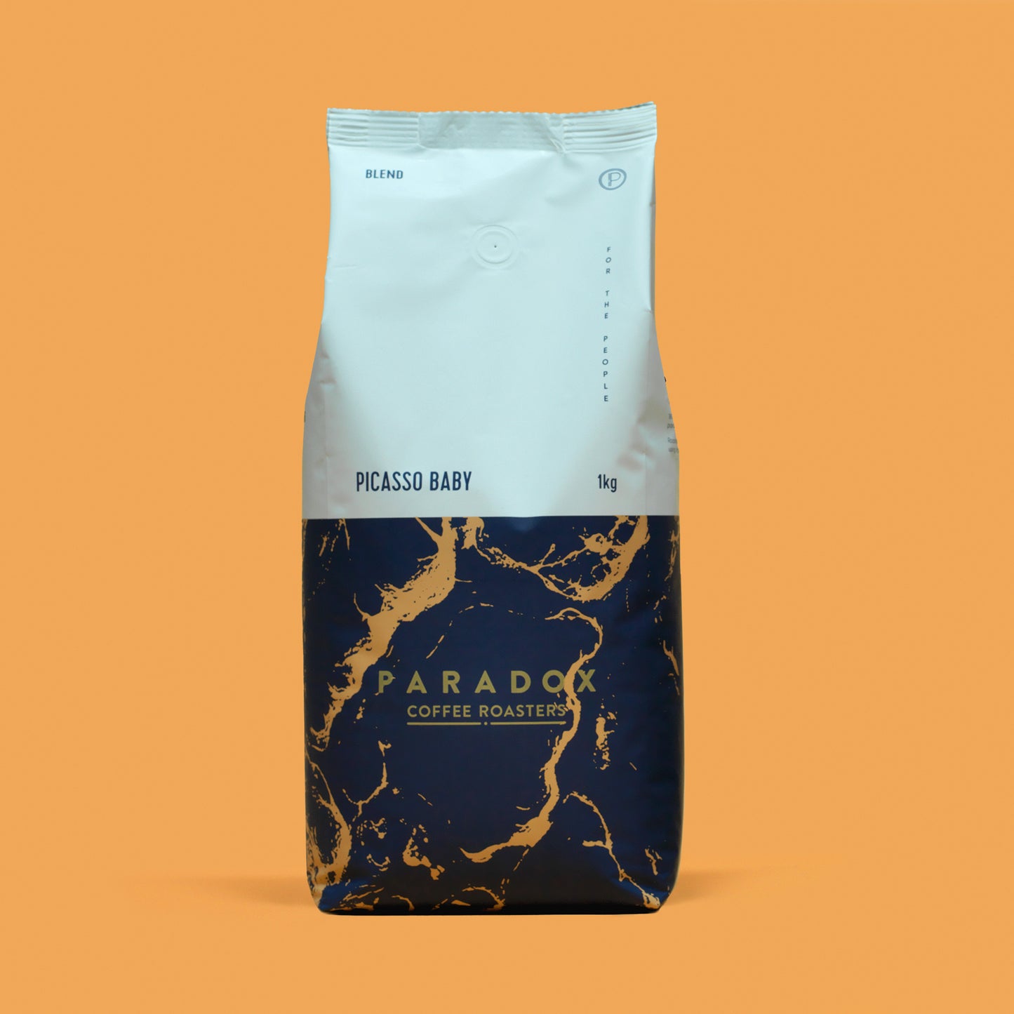 Roasted coffee beans from The Roast Collective. Paradox Coffee Roasters, Picasso Baby Blend. Image shows a tri-tone 1kg bag of the coffee against a nugget yellow background. The top half of the bag is white, with a navy blue and gold coloured pattern covering the bottom half of the bag. Paradox's logo is centred in the bottom half of the bag, with the lend name and weight at the bottom of the white section of the bag. 