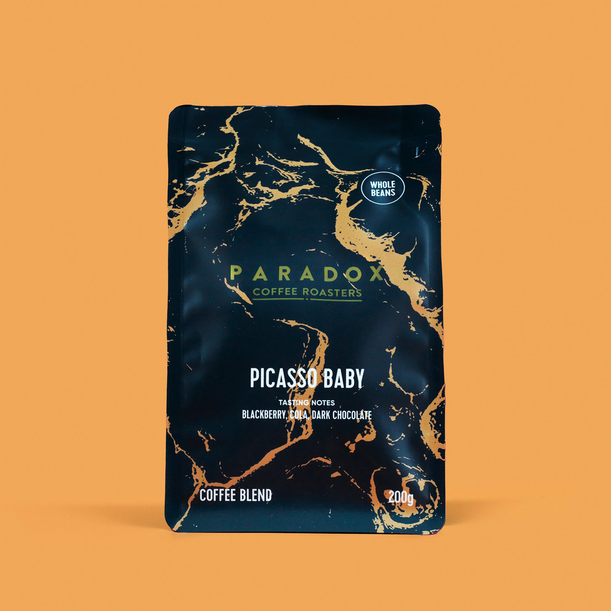 Roasted coffee beans from The Roast Collective. Paradox Coffee Roasters, Picasso Baby Blend. Image shows a 200g bag of the coffee against a nugget yellow coloured background. The bag is two-tone in colour, with navy blue and gold arranged in a geological print. Paradox's logo is centred in the top half of the bag, with the blend name, tasting notes and weight underneath. 