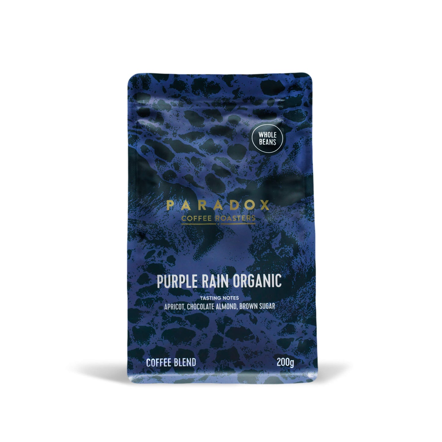 Roasted coffee beans from The Roast Collective. Paradox Coffee Roasters, Purple Rain Organic Blend. Image shows a 200g bag of the coffee against a white background. The bag is two-tone in colour, with deep purple and dark navy blue arranged in a reptile skin pattern. Paradox's logo is centred in the top half of the bag, with the blend name, tasting notes and weight underneath. 