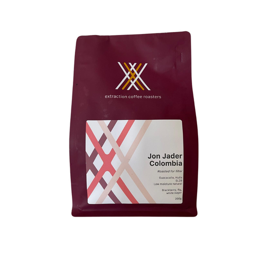 Extraction Coffee Roasters. Single Origin filter - roaster's choice. The image shows a 200g bag of coffee on a white background. The bag is maroon in colour, 'Extraction Coffee Roasters' branded, and feature's the roaster's triple X logo above the copy. The label shows a tri-coloured version of the roaster label and general coffee information such as producer, roast profile, tasting notes and coffee varietal. This bag is an example only. The Roast Collective.