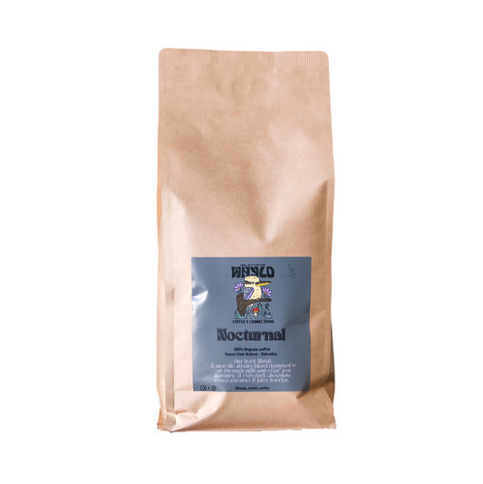 Roasted coffee beans from The Roast Collective. That's Whyld Coffee Roasters, Nocturnal Organic Blend. Image shows a brown 1kg bag of Nocturnal blend against a white background. The bag has a grey blue label centred on the lower half of the bag with the roaster's logo, blend name, and blend details on it. 