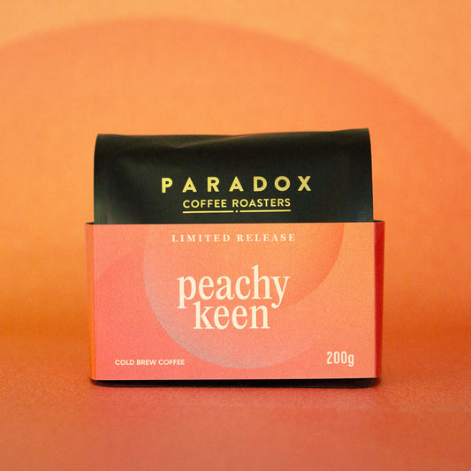 Roasted coffee beans Paradox Coffee Roasters Limited Edition: Peachy Keen 200g bag Cold Brew Coffee. Peach and orange coloured background. The Roast Collective.