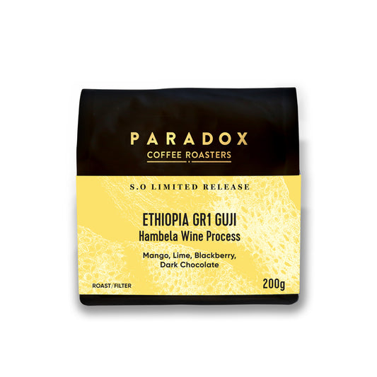 Roasted coffee beans from The Roast Collective. Paradox Coffee Roasters, Limited Release Ethiopia Guji Hambela Wine Process. Image shows a black 200g bag of the coffee against a white background. The bag has Paradox's logo centred at the top of the bag in gold coloured print and a sunflower yellow label centred on the lower half of the bag with the product name, tasting notes, roast profile and weight on it.