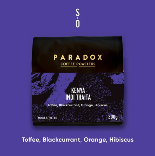 A package of Paradox Coffee Roasters Kenya Inoi Thaita coffee on a solid purple background, with the text 'TOFFEE, BLACKCURRANT, ORANGE, HIBISCUS' below.