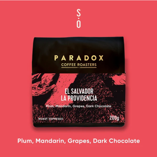 A 200g bag of Paradox Coffee Roasters 'El Salvador La Providencia' espresso coffee, featuring a black and red textured design, set against a solid coral-pink background with white text overlays.